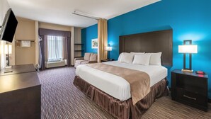 A hotel room with a large bed, a desk, a TV, and a window with curtains. - Residency Suites - Cotulla (Cotulla)