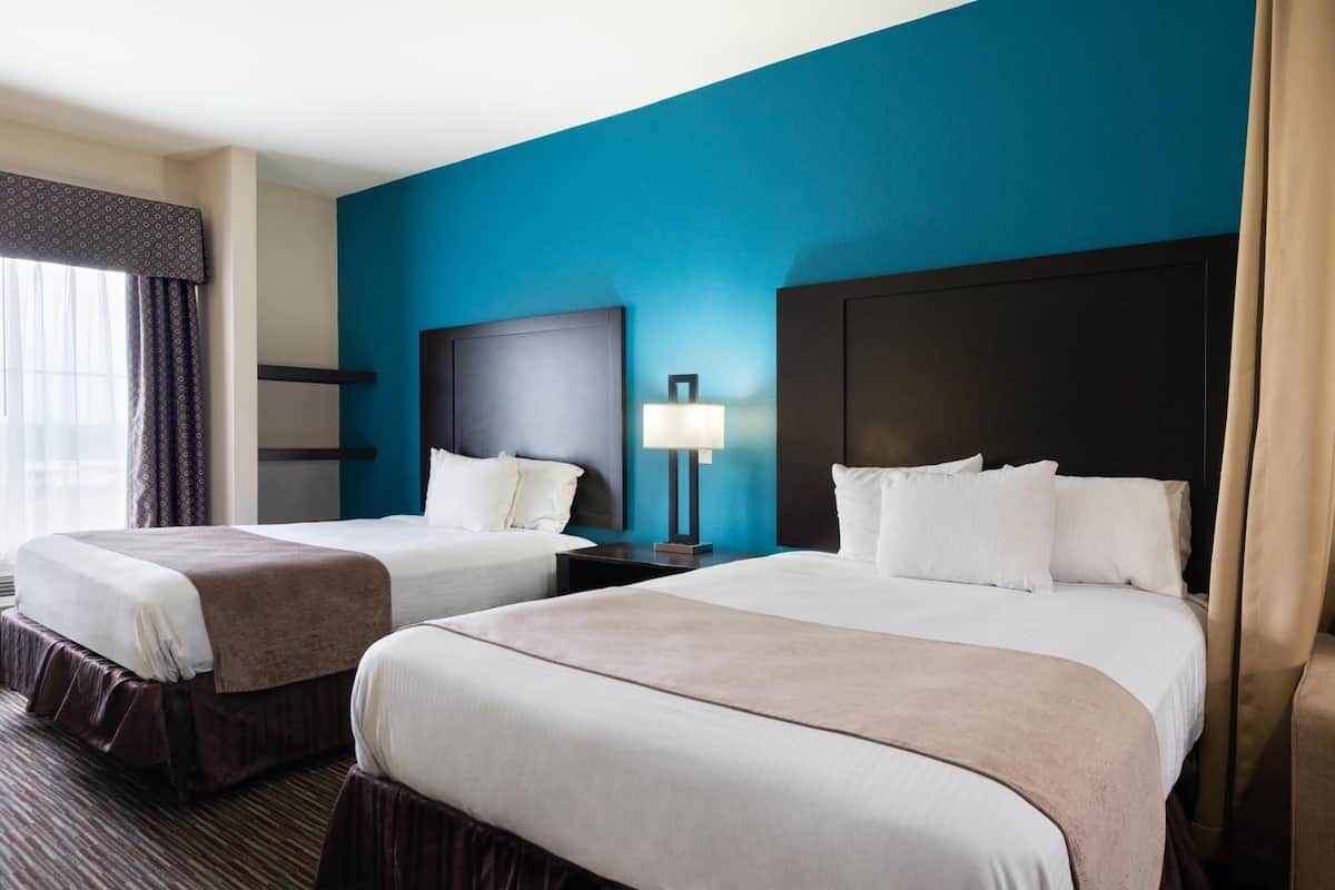 Une chambre d’hôtel avec deux lits, un mur d’accent bleu et une fenêtre avec des rideaux.