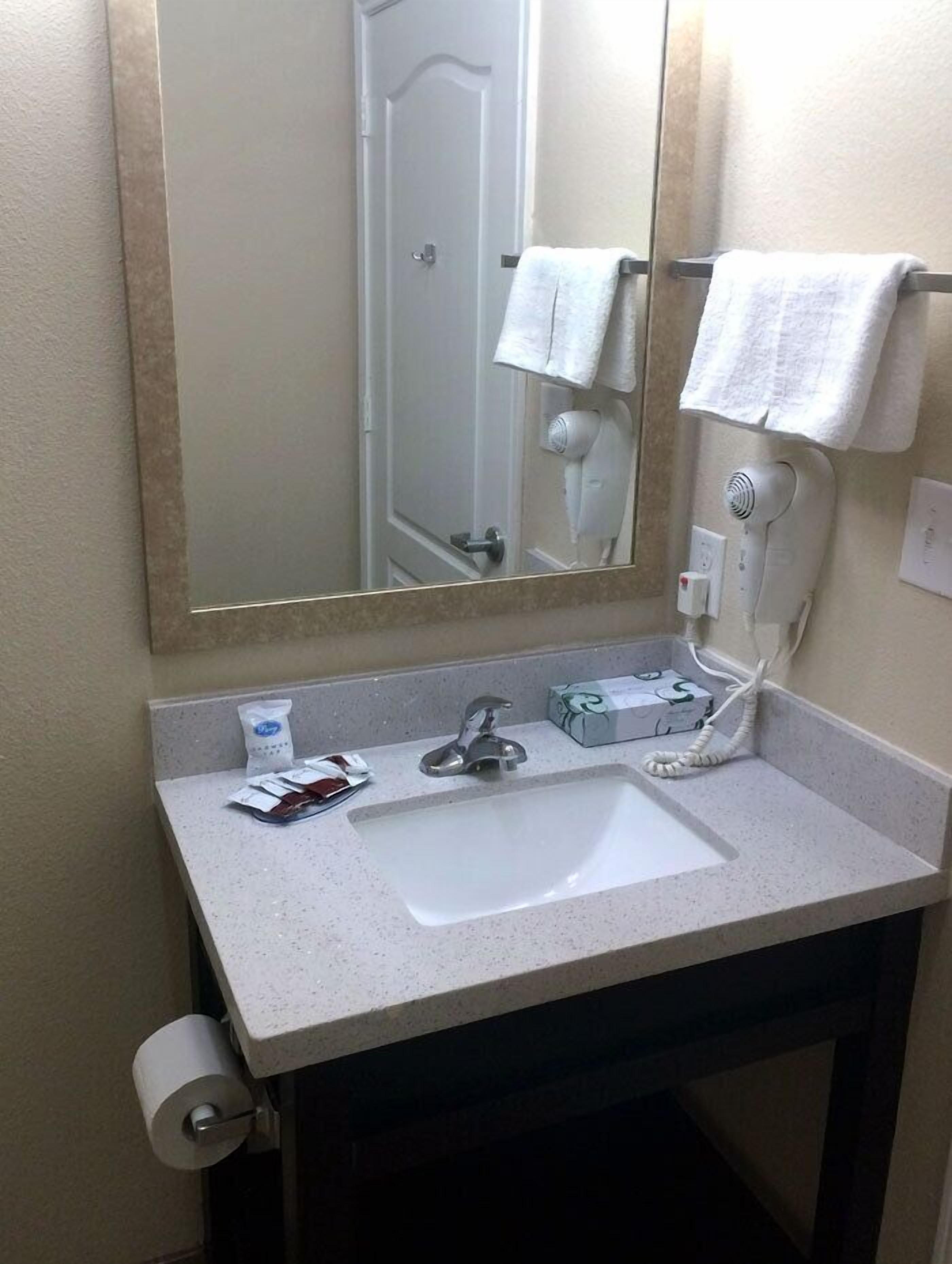 A bathroom with a sink, mirror, towel rack, hairdryer, and toiletries.