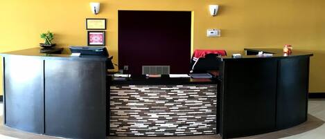 A reception desk with a modern design, featuring a black and white patterned wall, framed certificates on the wall, and a small plant on the desk.