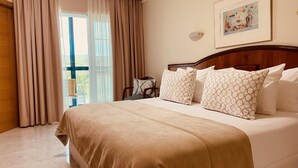 Habitación de hotel con una cama grande, cortinas color beige, cabecera de madera y un cuadro en la pared.