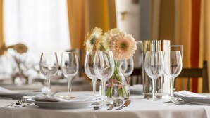 Una mesa de comedor dispuesta con varias copas de vino, platos y cubiertos, con un florero en el centro.