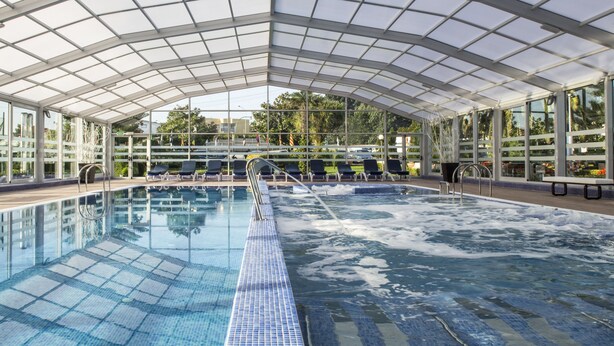 Una piscina interior con techo de cristal, múltiples sillones de descanso y vistas despejadas de la vegetación circundante.