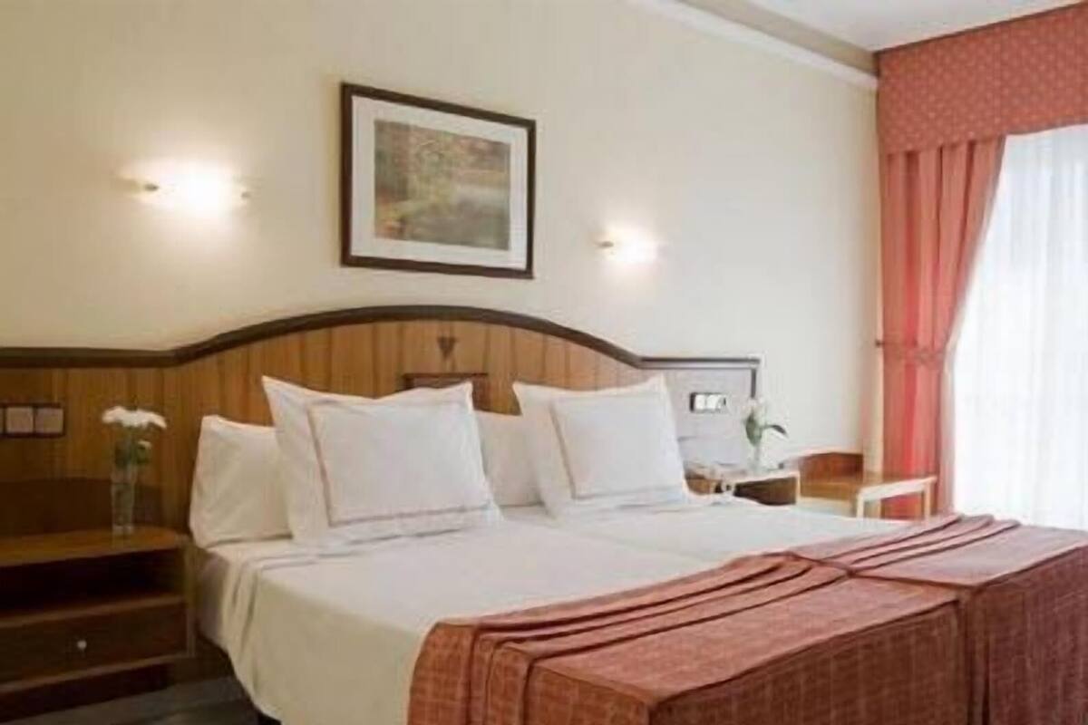 Une chambre d’hôtel avec un lit, une table de chevet, un tableau encadré au mur et une fenêtre avec des rideaux.