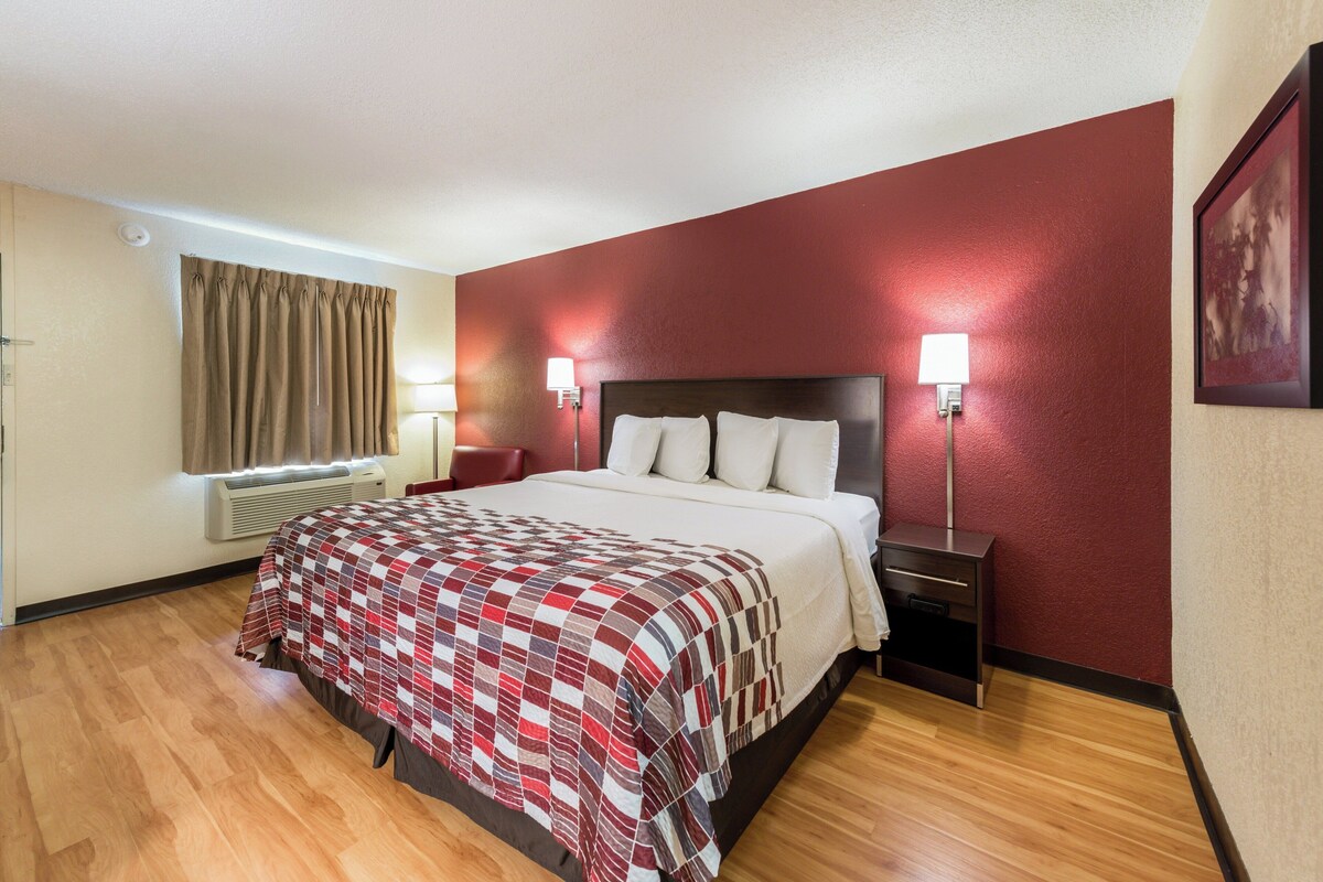 A hotel room with a bed, bedside lamps, a heater, and a window with curtains.