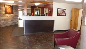 A reception area with a stone wall, a Red Roof Inn sign, a reception desk, and red seating. - Red Roof Inn Grand Junction (Grand Junction)