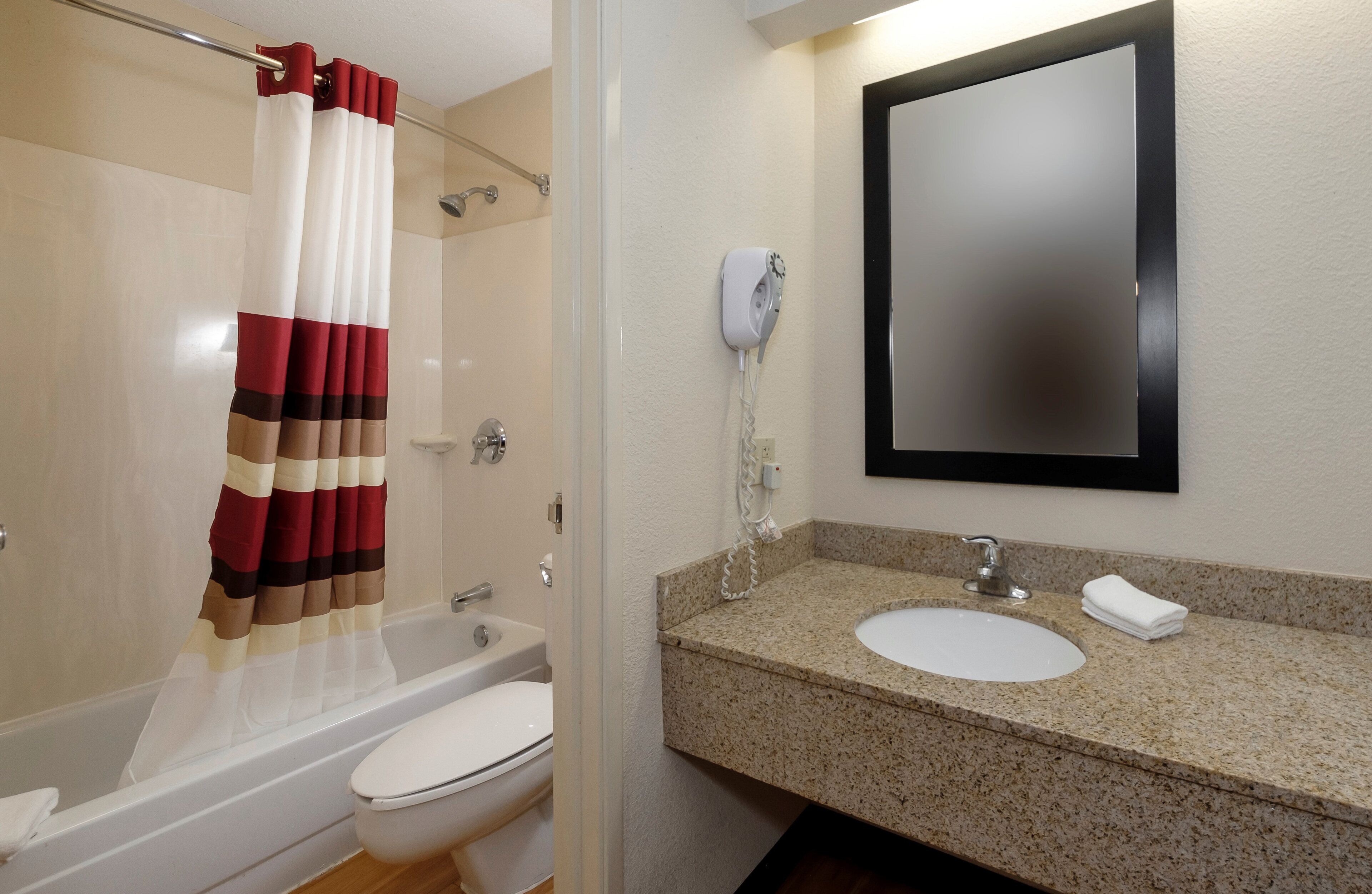 Un baño con cortina de ducha, inodoro, lavabo con espejo y teléfono.