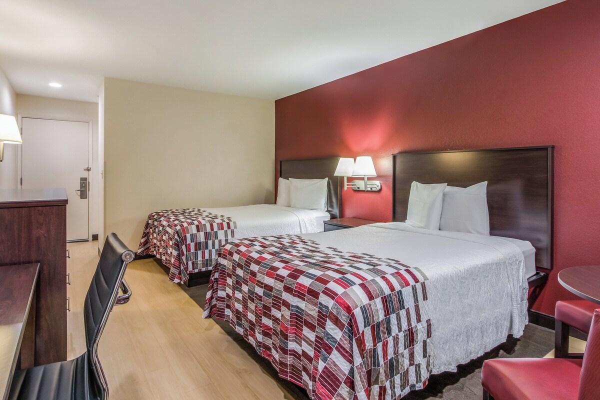 A hotel room with two beds, a desk, and a chair.
