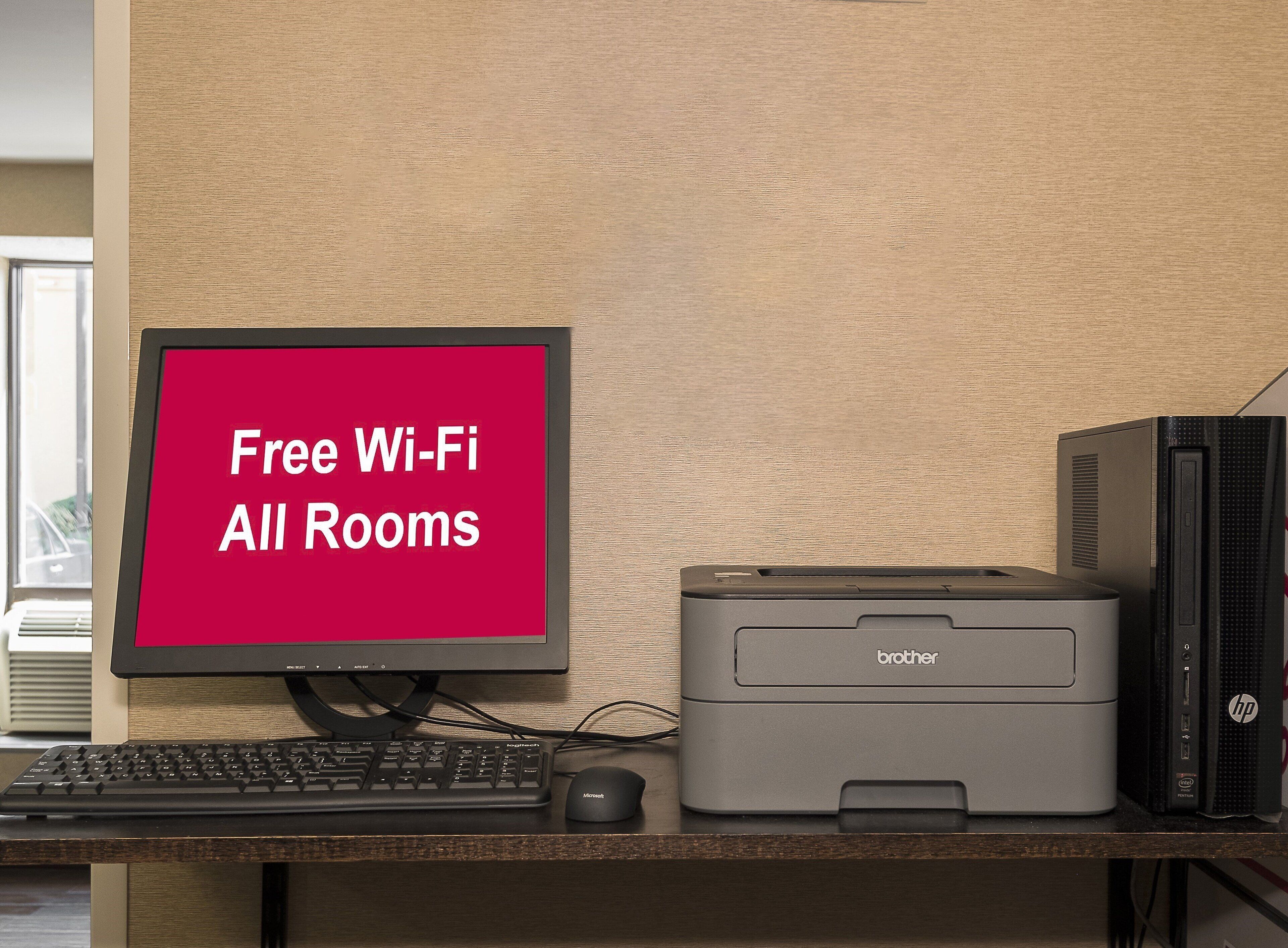 Un ordinateur de bureau comprenant un écran affichant la mention « Wi-Fi gratuit dans toutes les chambres », un clavier, une souris et une imprimante.
