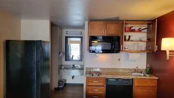 Cocina compacta con refrigerador, microondas, lavamanos y armarios de madera.