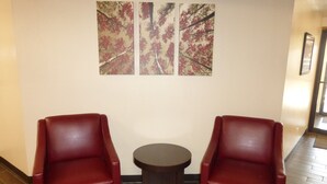 A seating area with two red chairs and a small round table, with a wall-mounted artwork above. - Red Roof Inn Grand Junction (Grand Junction)
