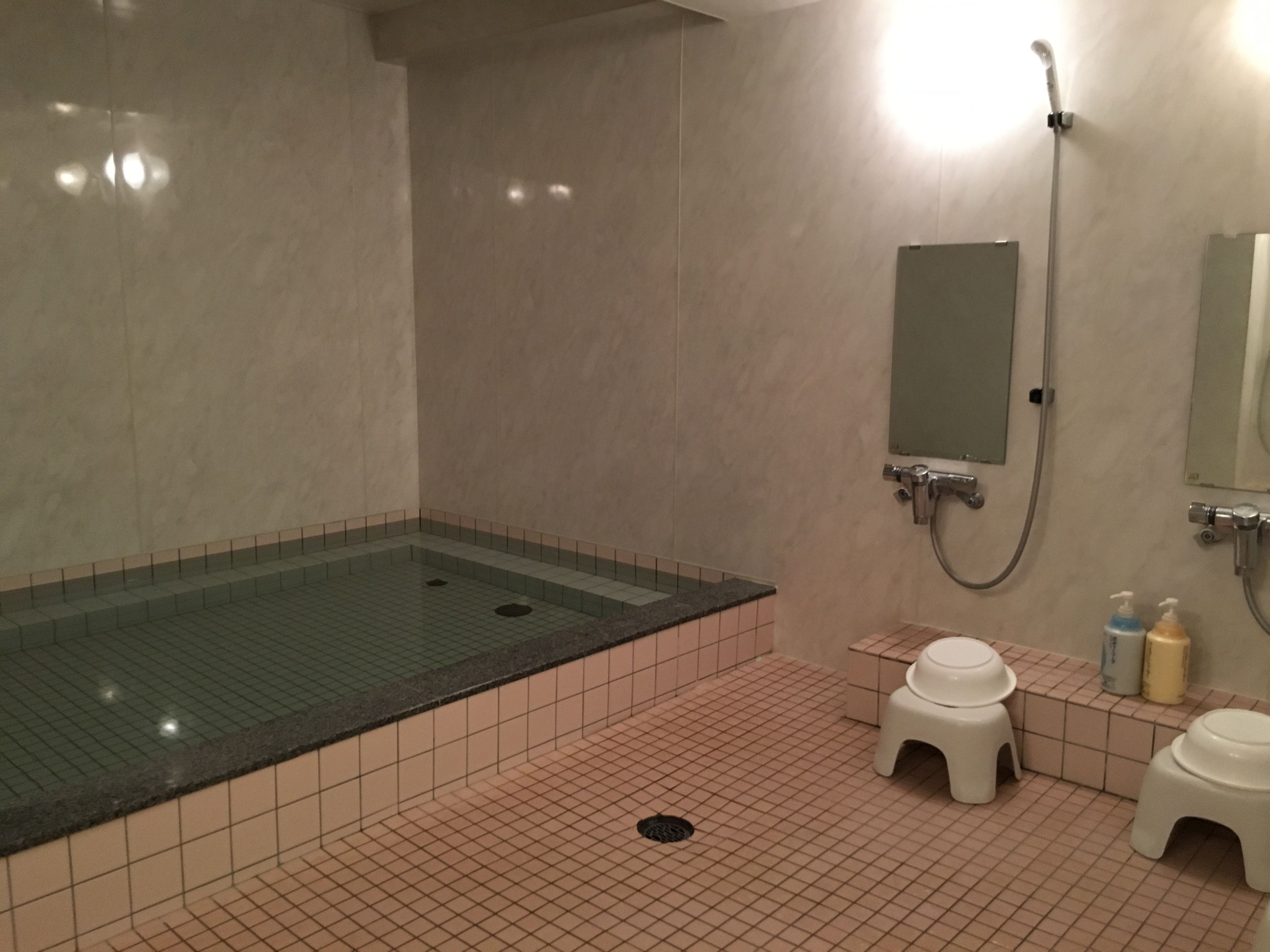 Een badkamer met een bubbelbad in een glazen ombouw, een douche, een wastafel en een spiegel.