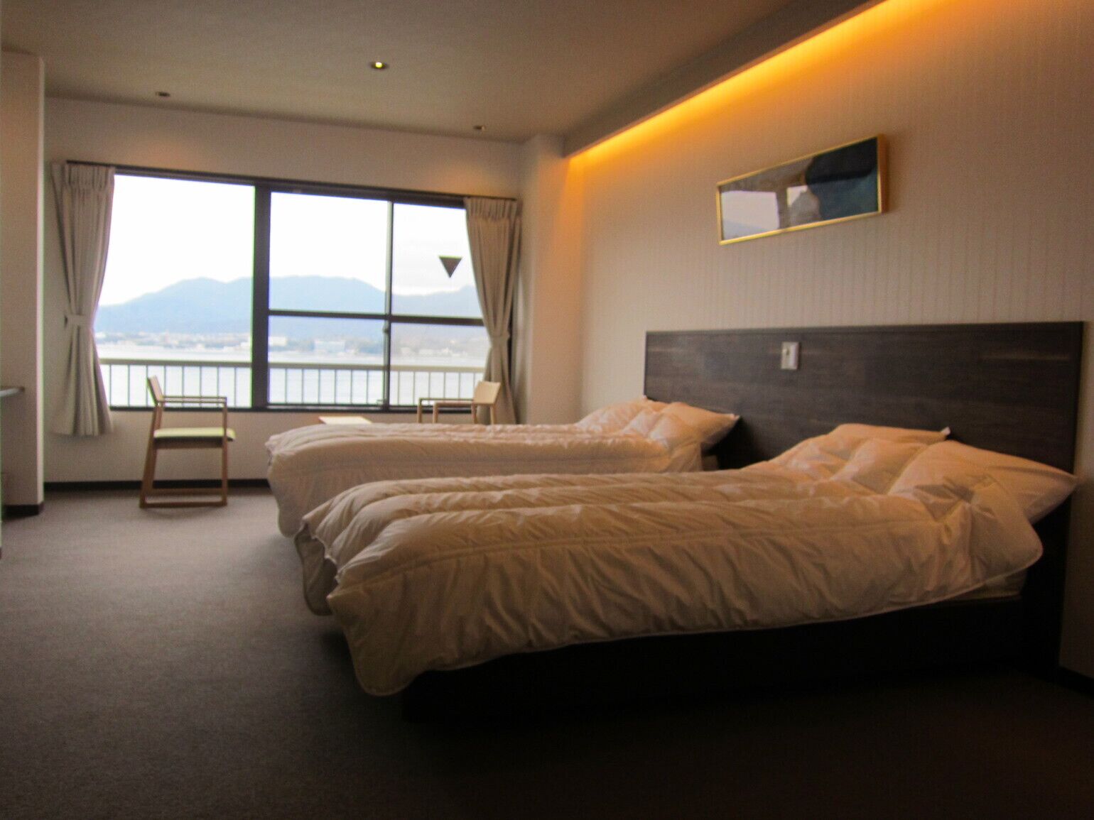 Une chambre d’hôtel avec deux lits, une chaise, une fenêtre donnant sur un paysage agréable et un miroir au mur.