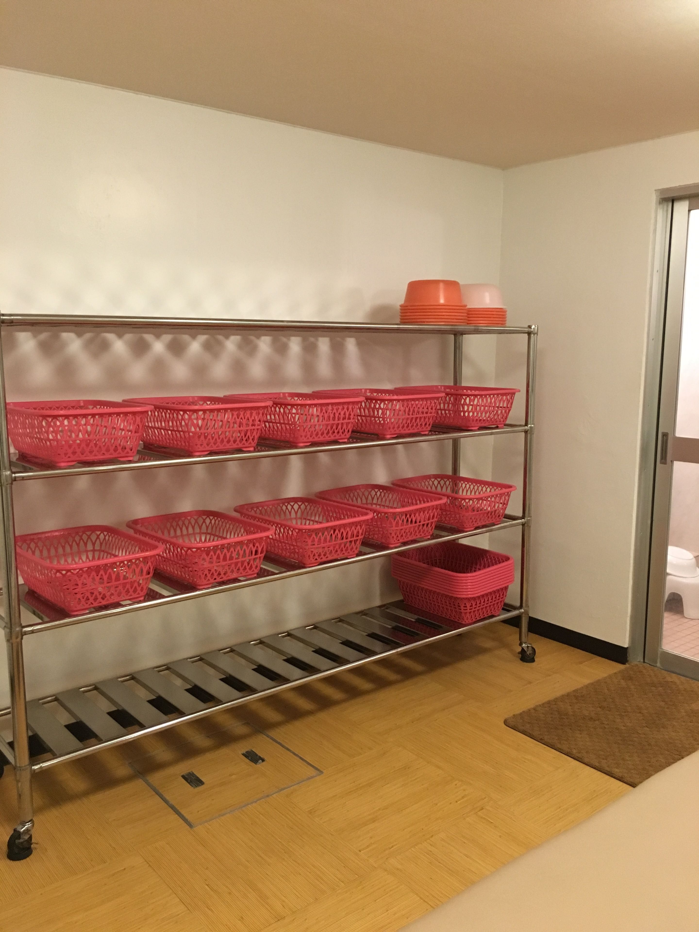 A metal shelving unit with pink baskets and orange containers.