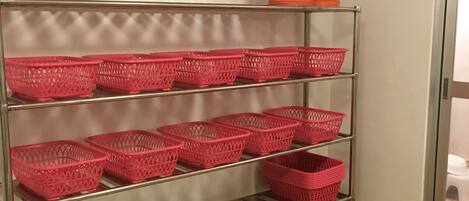 A metal shelving unit with pink baskets and orange containers.