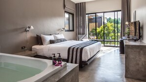 A modern hotel room with a large bed, a bathtub, and a balcony with a view of greenery.