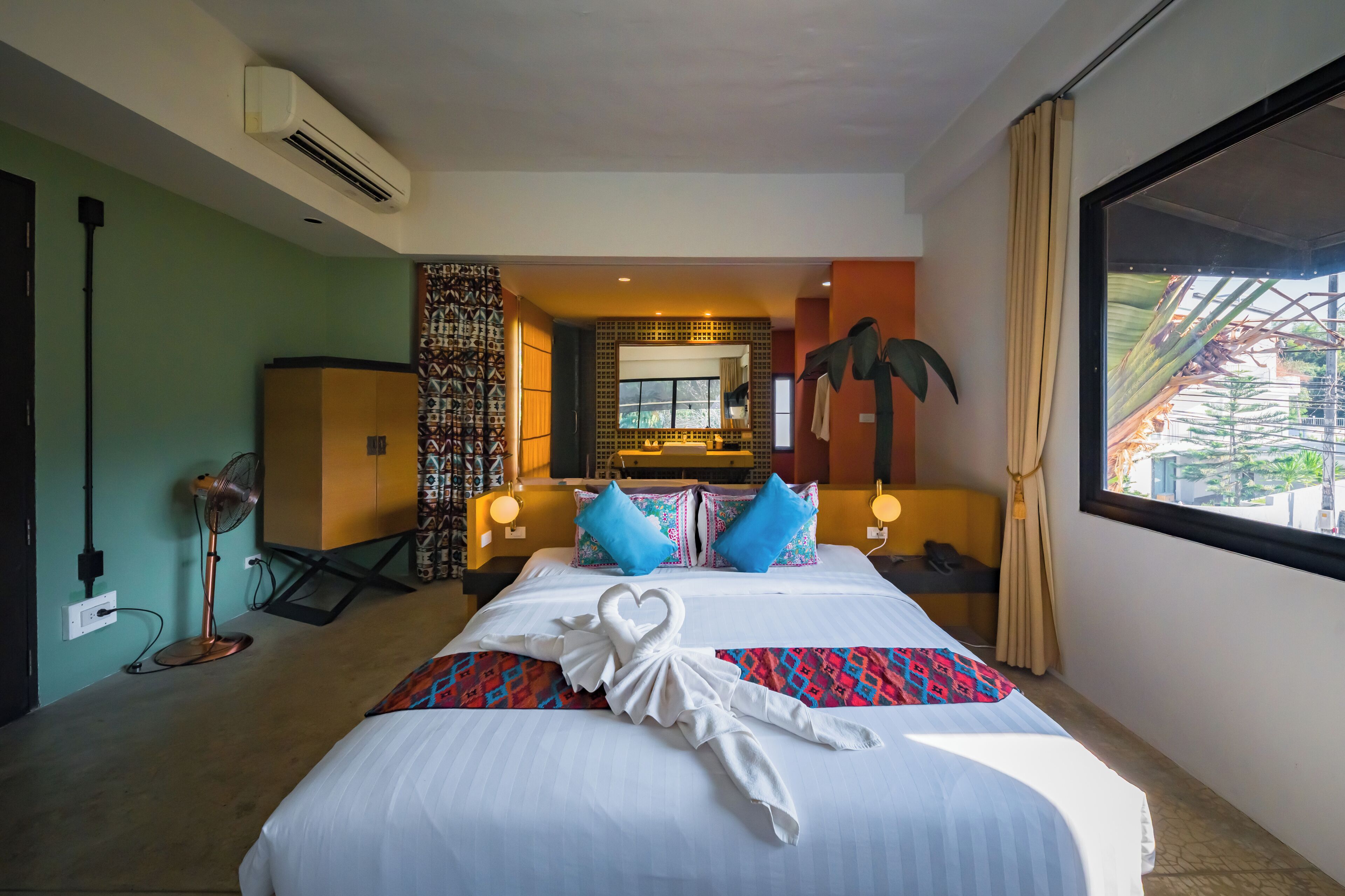 Quarto de hotel com cama, espelho, ventilador e vista para o exterior.