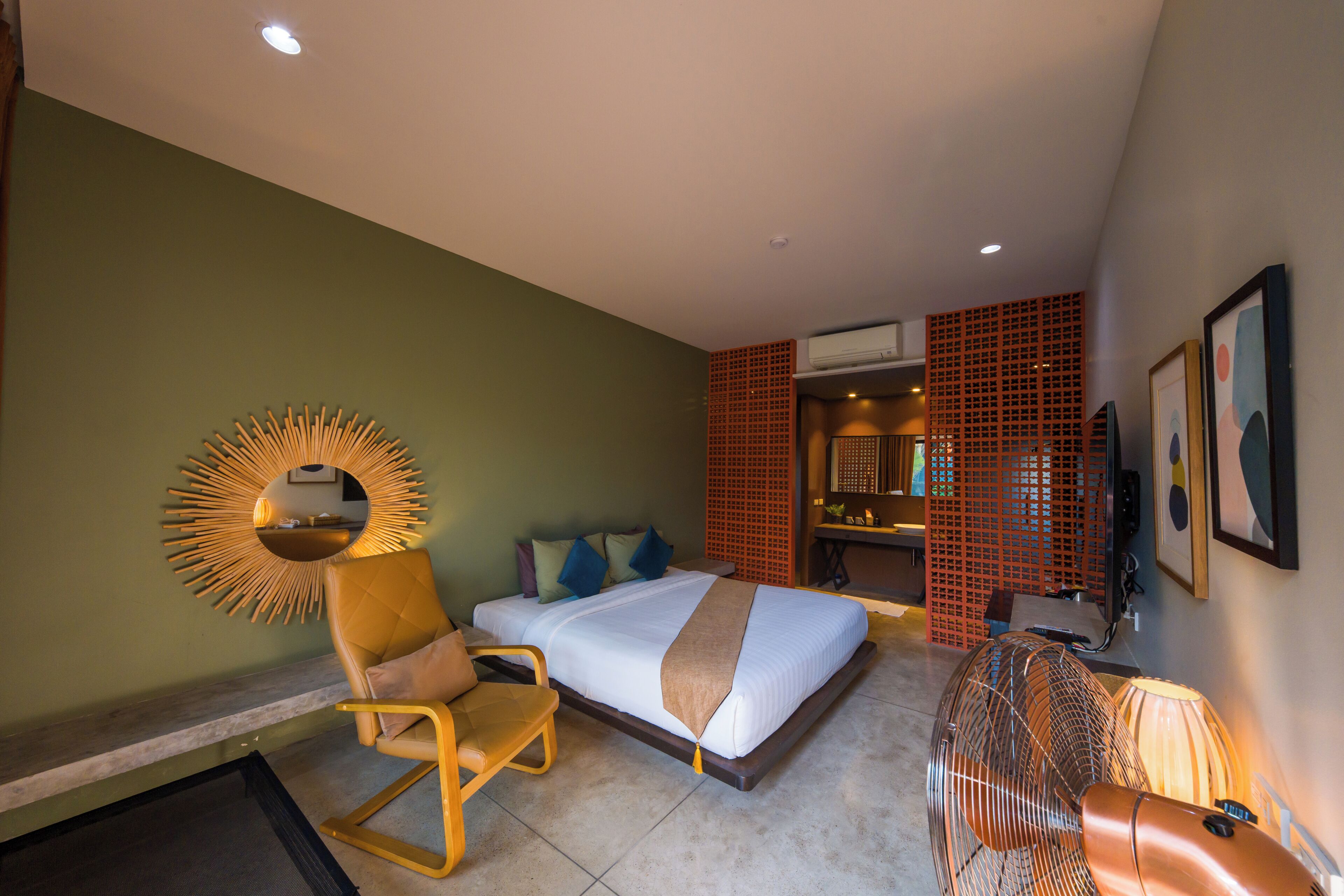 A hotel room with a bed, a chair, a fan, and a mirror on the wall.