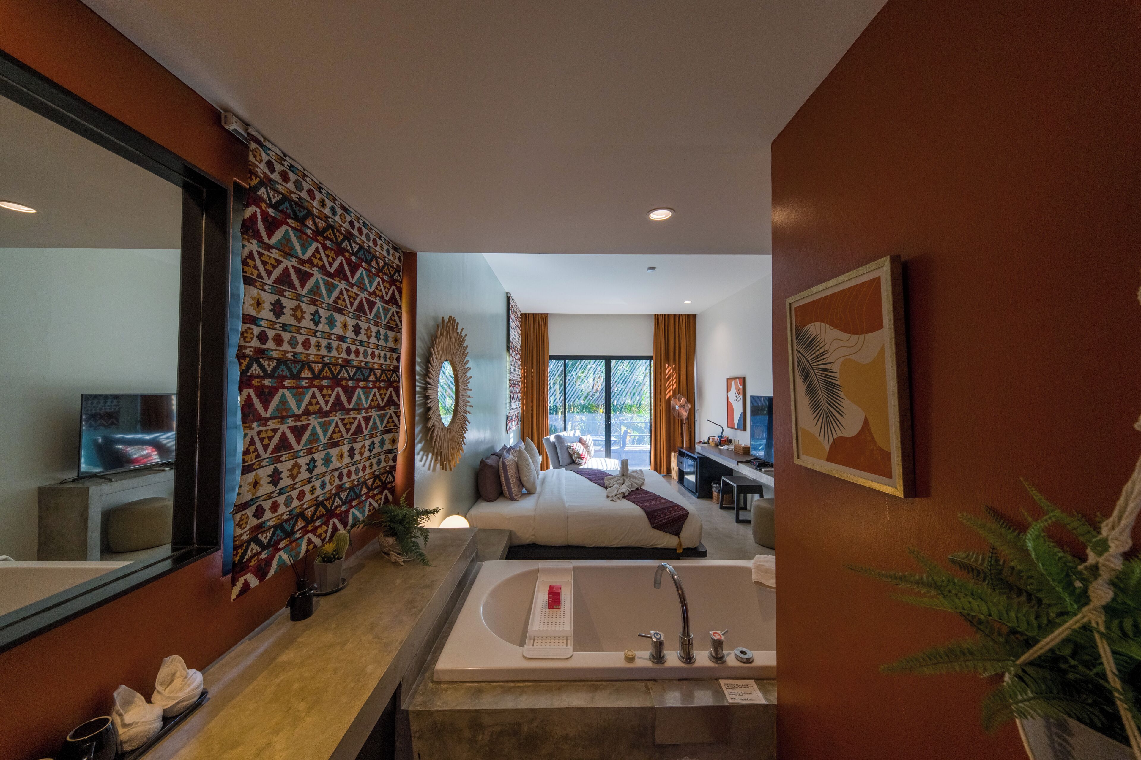 A hotel room with a large bed, a bathroom with a bathtub, a desk, and a large mirror.