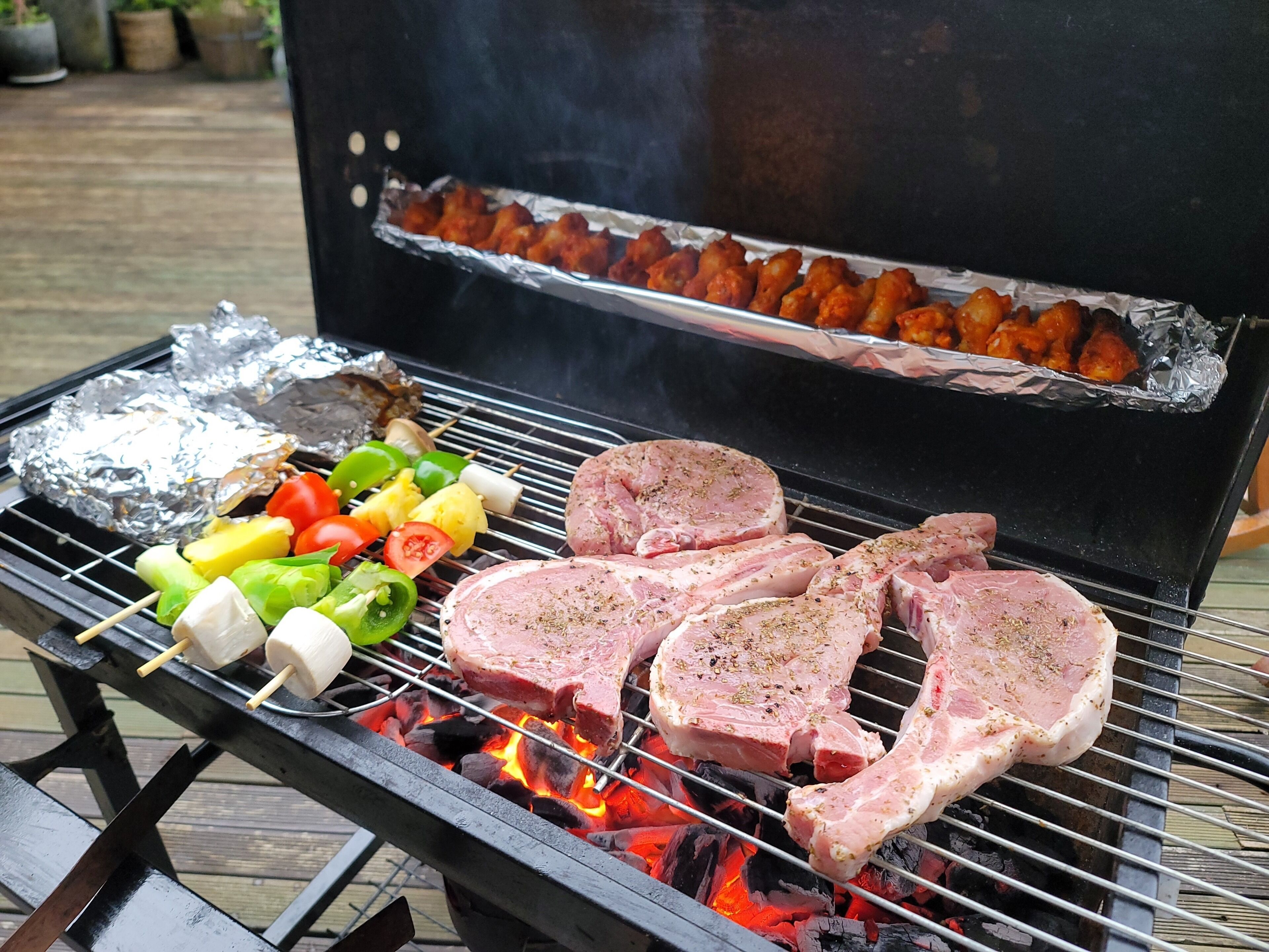 Un barbecue avec des brochettes de légumes et de viande, ainsi que des aliments enveloppés dans du papier d’aluminium.