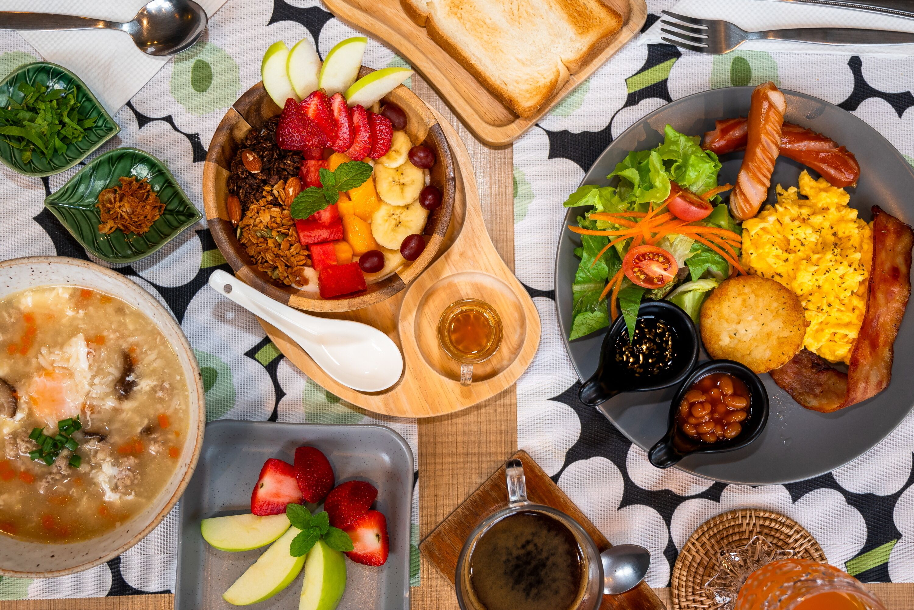 A table with various dishes including soup, salad, toast, and a plate with eggs, bacon, and sausages.