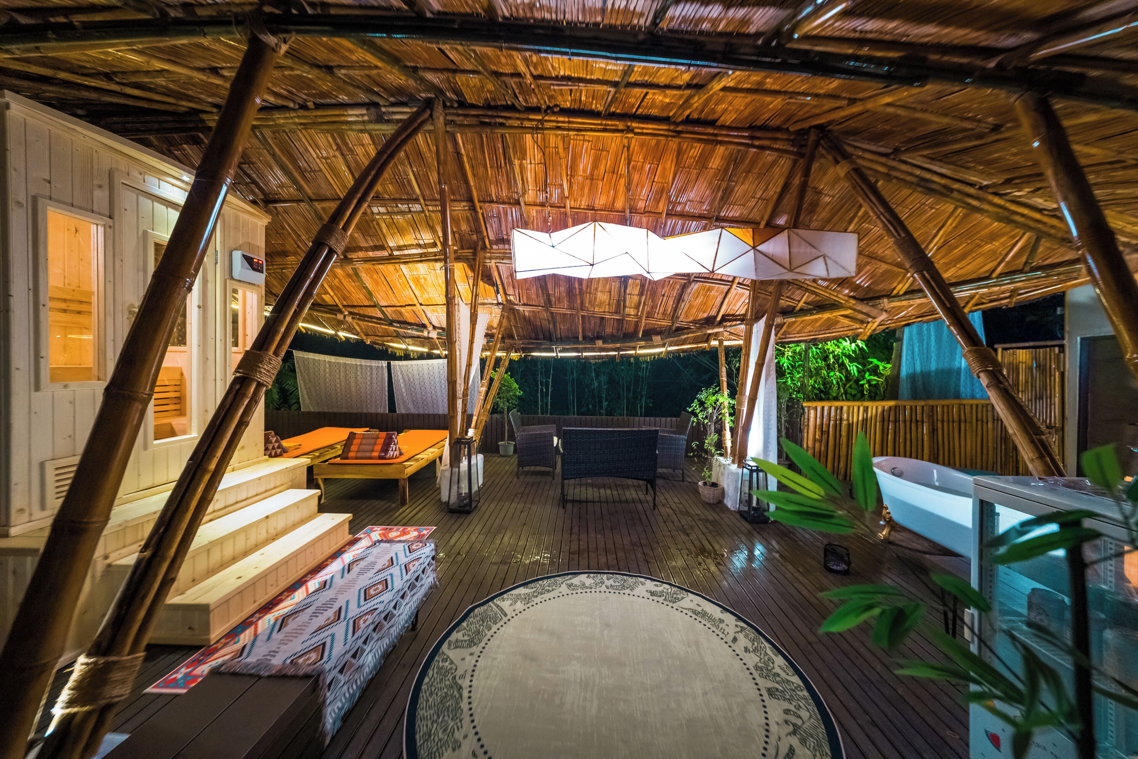 Un espacio al aire libre cubierto con una terraza de madera, una bañera blanca y un área de estar con una mesa y sillas.