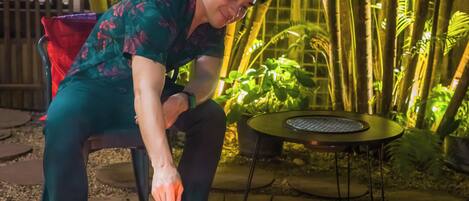 A person roasting marshmallows over a fire pit in an outdoor setting with bamboo plants.
