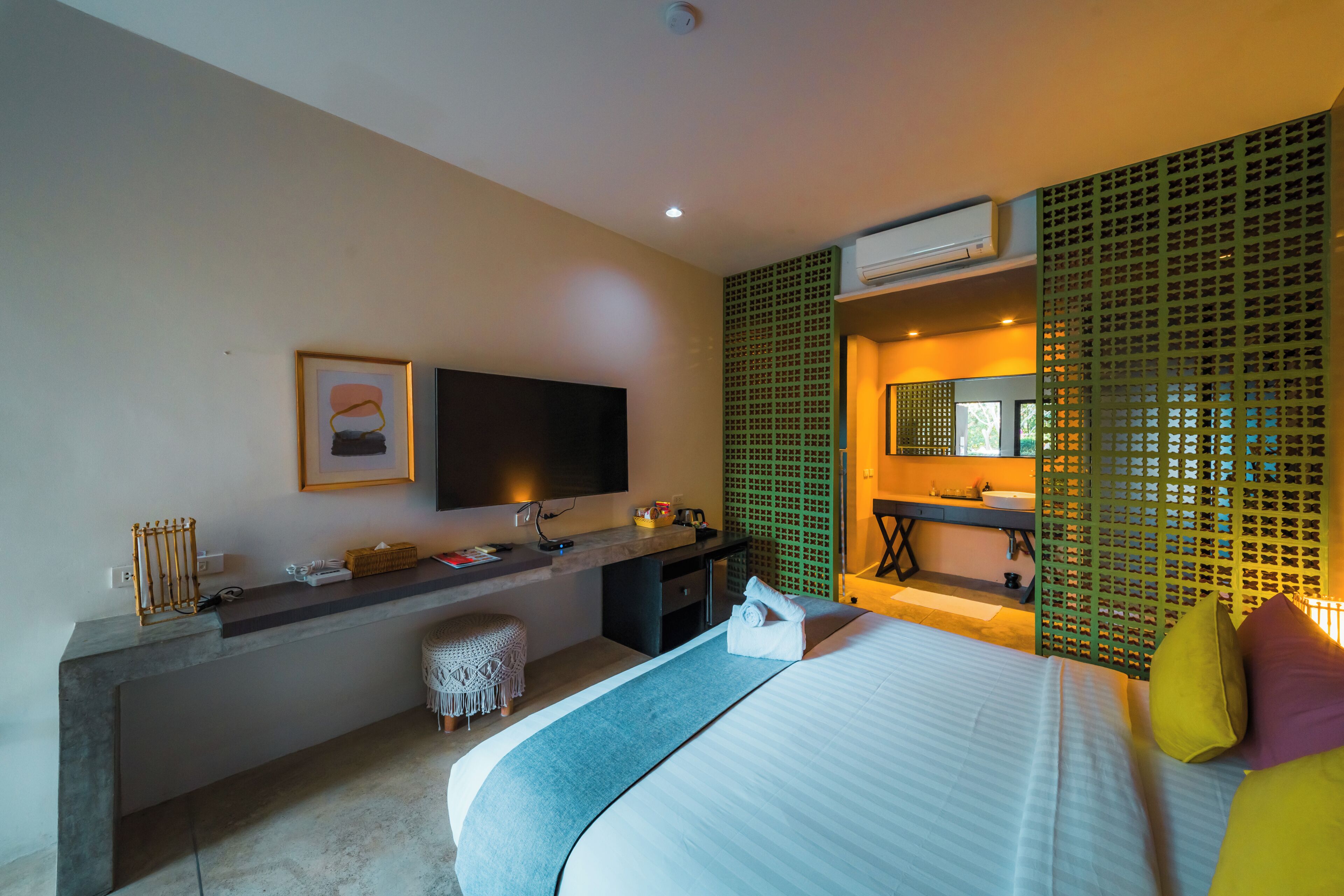 A modern hotel room with a bed, a desk, a television, and a bathroom.