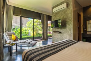A modern hotel room with a large bed, a sofa, a TV mounted on the wall, and a balcony with a view of greenery.