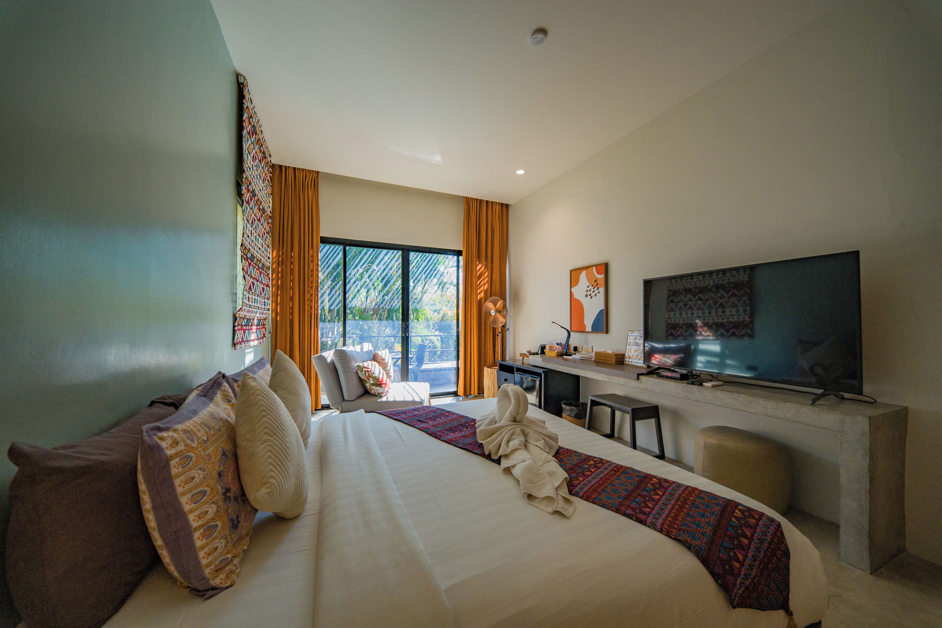 A hotel room with a large bed, a desk, a television, and a view of the outdoors.