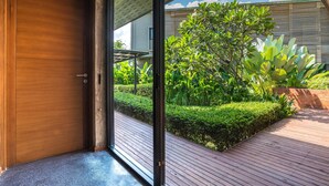 Una entrada moderna con una puerta de madera que da a una terraza de madera y un jardín con diversas plantas.