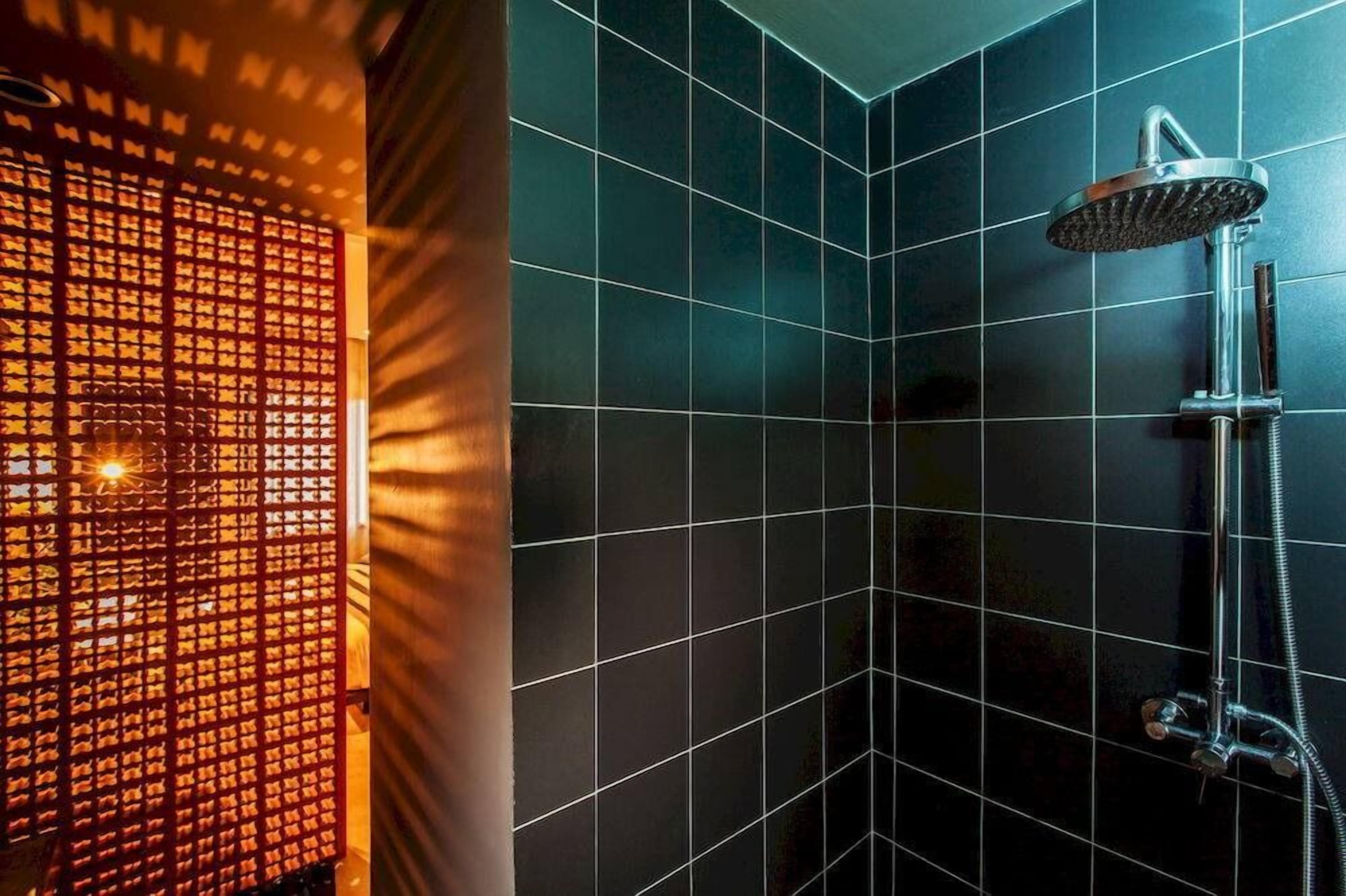 A bathroom with dark tiled walls, a shower with a handheld showerhead, and a visible towel rack.