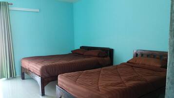 A room with two single beds, a wooden headboard, a light blue wall, and a curtain on the left.