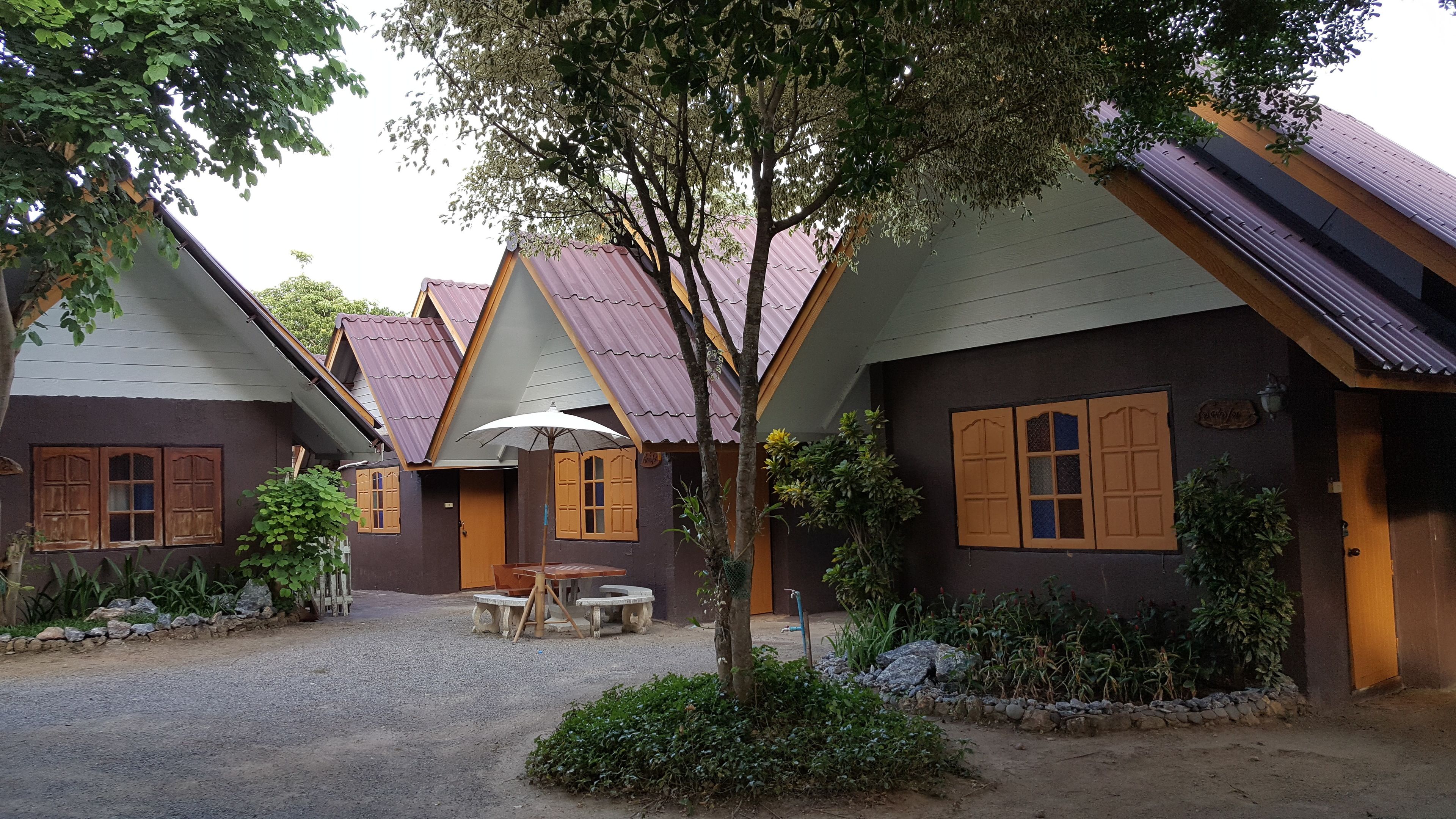 A row of traditional-style cottages with pitched roofs and wooden shutters, a gravel courtyard, and a small table with an umbrella.