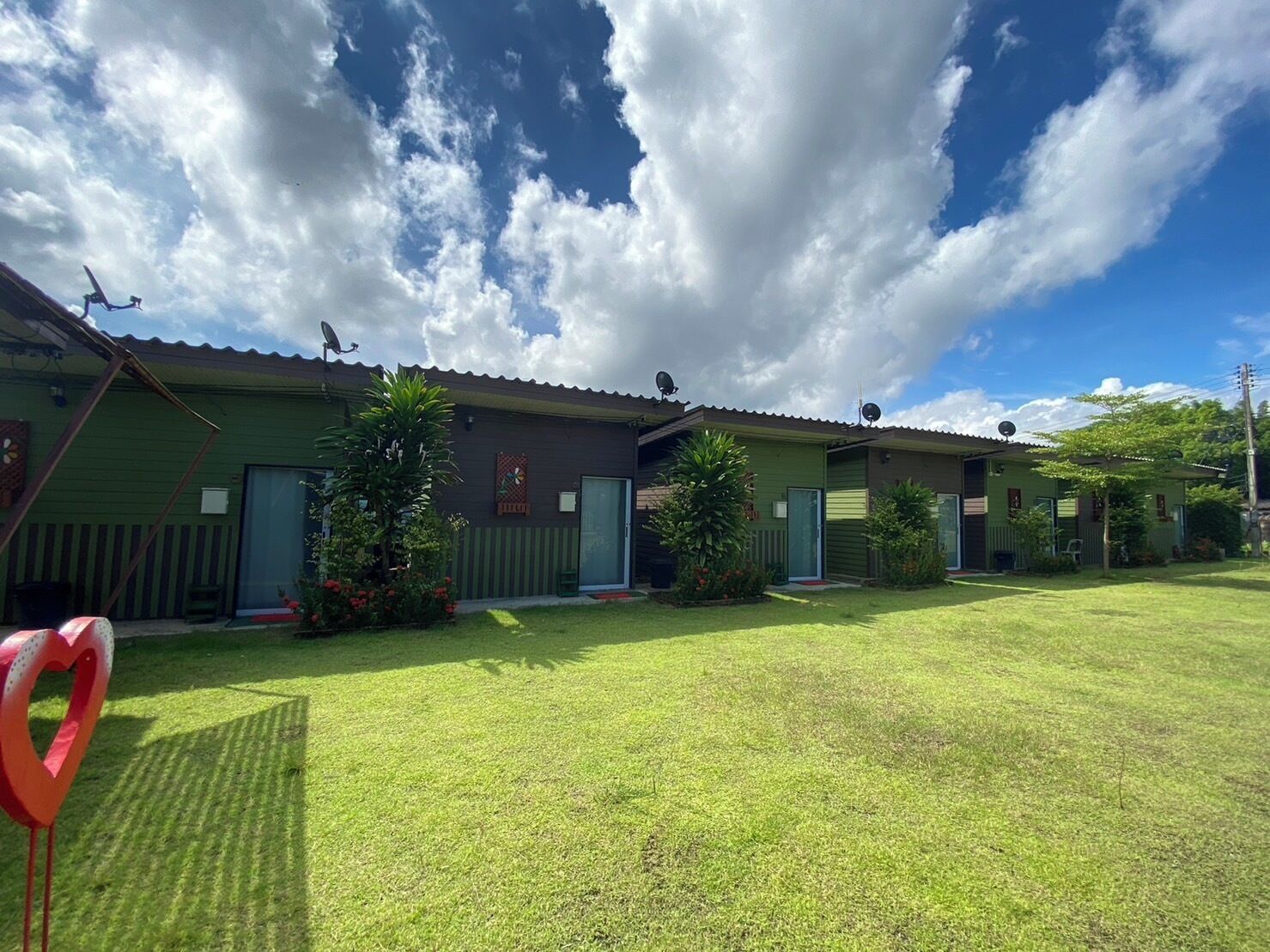 A row of green buildings with satellite dishes, a heart-shaped decoration, and a clear sky.