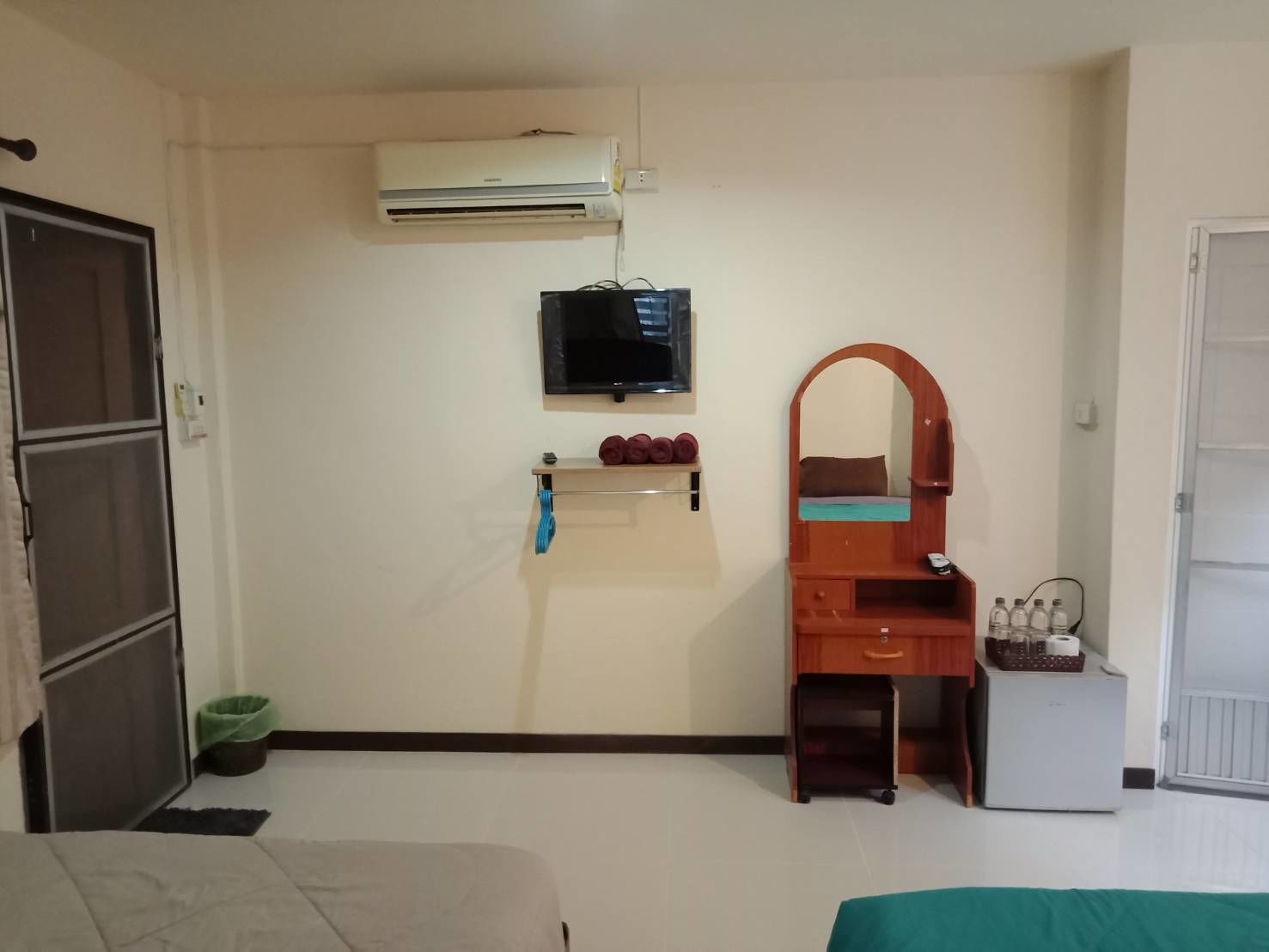 A room with a bed, a desk with a mirror, a television, and a small refrigerator.