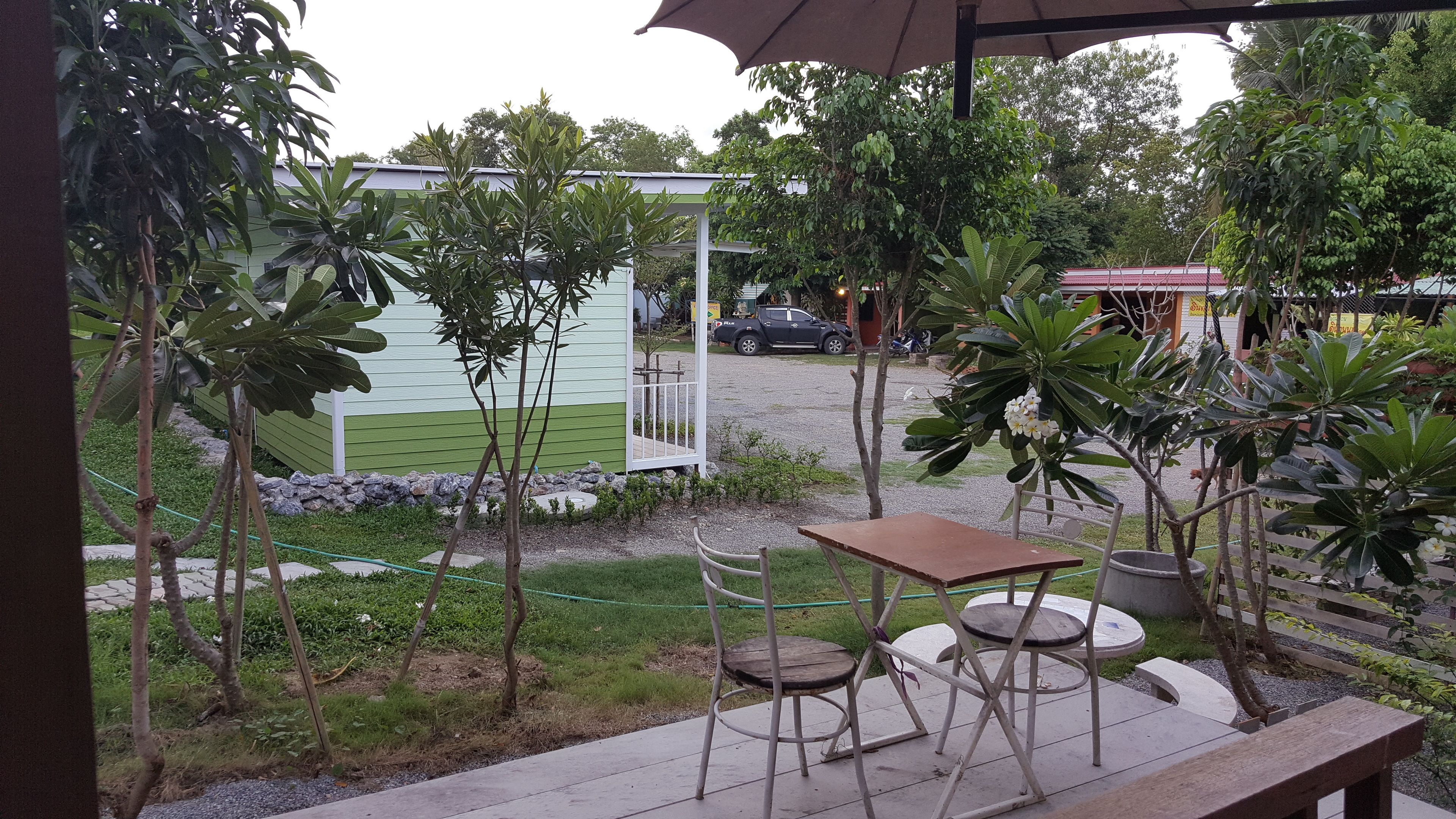 A patio area with a table and chairs, surrounded by greenery and a view of a building with a green roof.