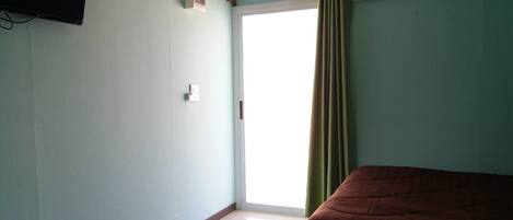 Una habitación con una cama, una ventana con cortina y un aire acondicionado instalado en la pared.