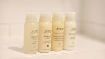 Four bottles of Aveda products on a white shelf.