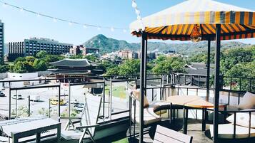 A rooftop terrace with outdoor seating, a traditional Korean pavilion, and a view of the cityscape and hills.