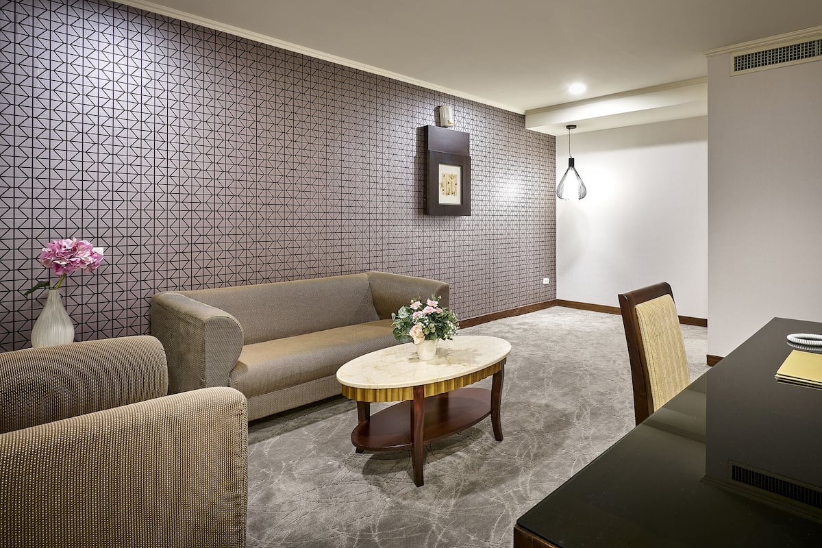 A modern living room with a patterned wallpaper, a sofa, a round coffee table with flowers, a dining table with a phone, and a chair.