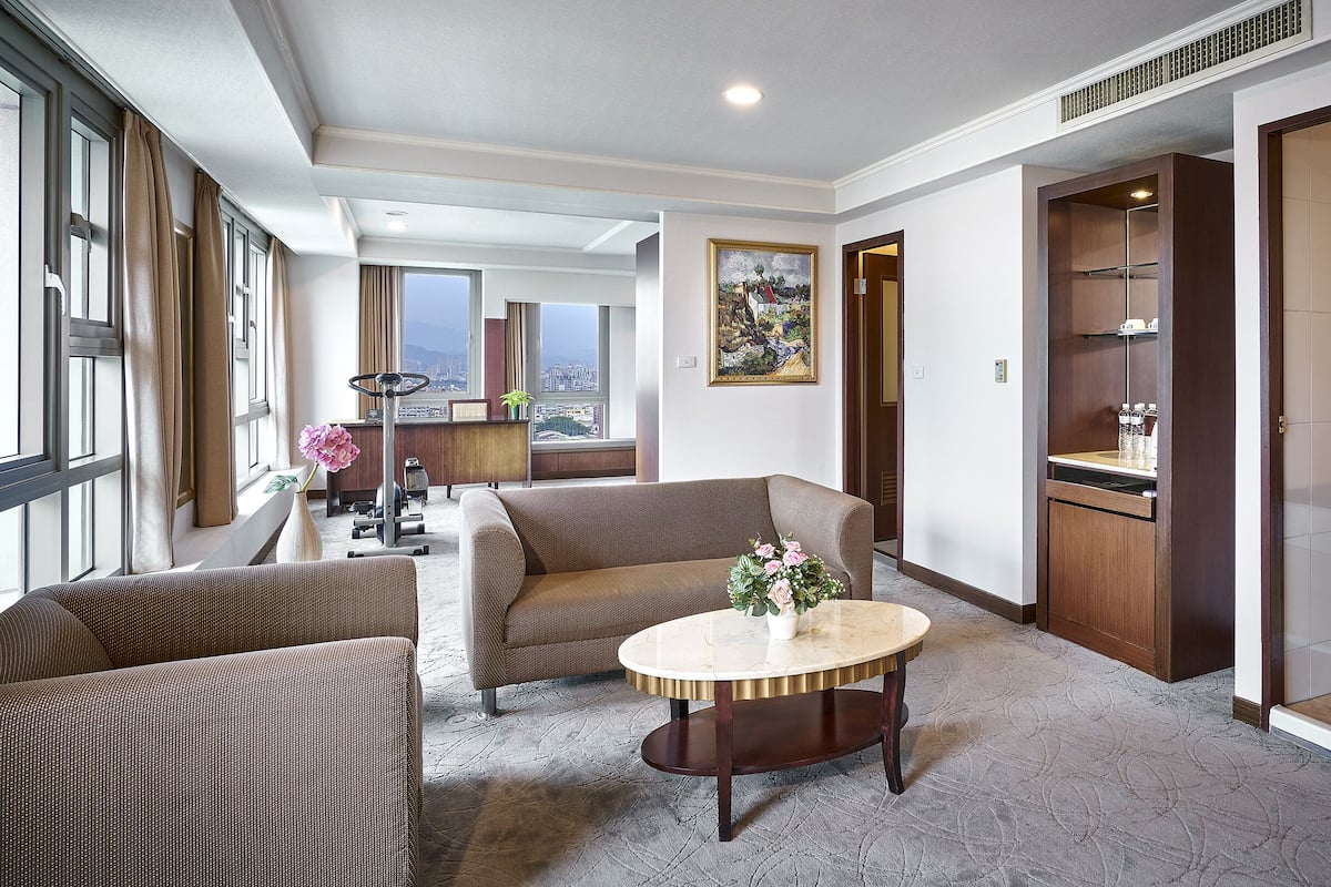 A modern living room with a sofa, a round coffee table with a vase, and a view of the city through large windows.