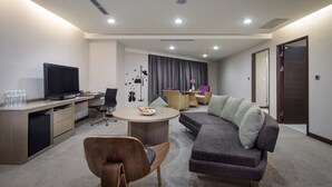 Una habitación de hotel moderna con televisión de pantalla plana, una mesa de comedor, un sofá y un escritorio con computadora.