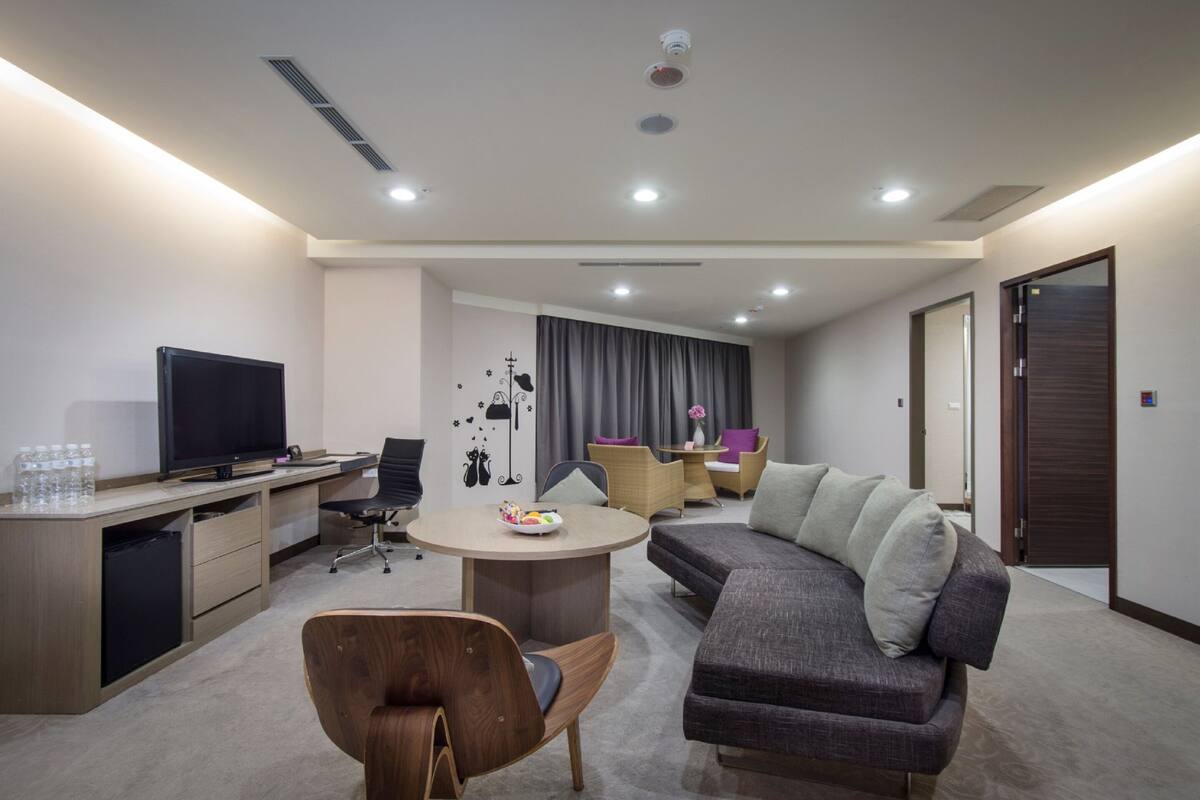 A modern hotel room with a flat-screen TV, a dining table, a sofa, and a desk with a computer.