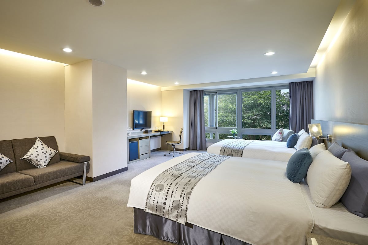 A hotel room with a sofa, a desk, a television, and a bed with multiple pillows.