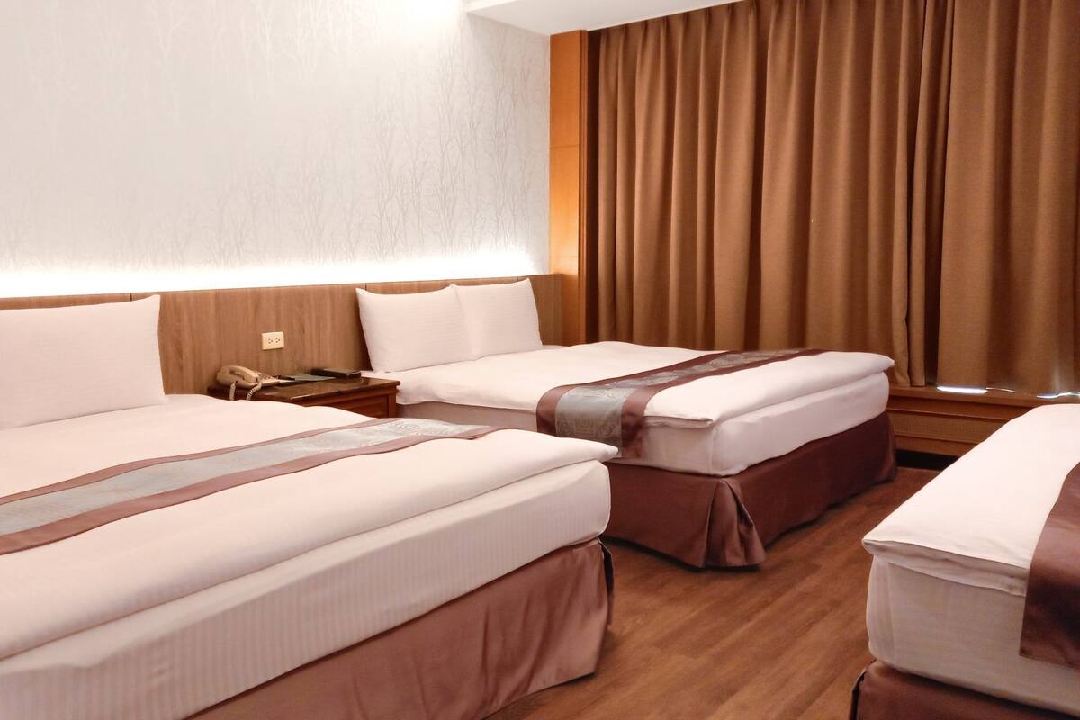 A hotel room with two beds, a bedside table with a phone, and a window with curtains.