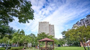 Un parque con un pabellón, césped verde, árboles y un edificio alto al fondo.