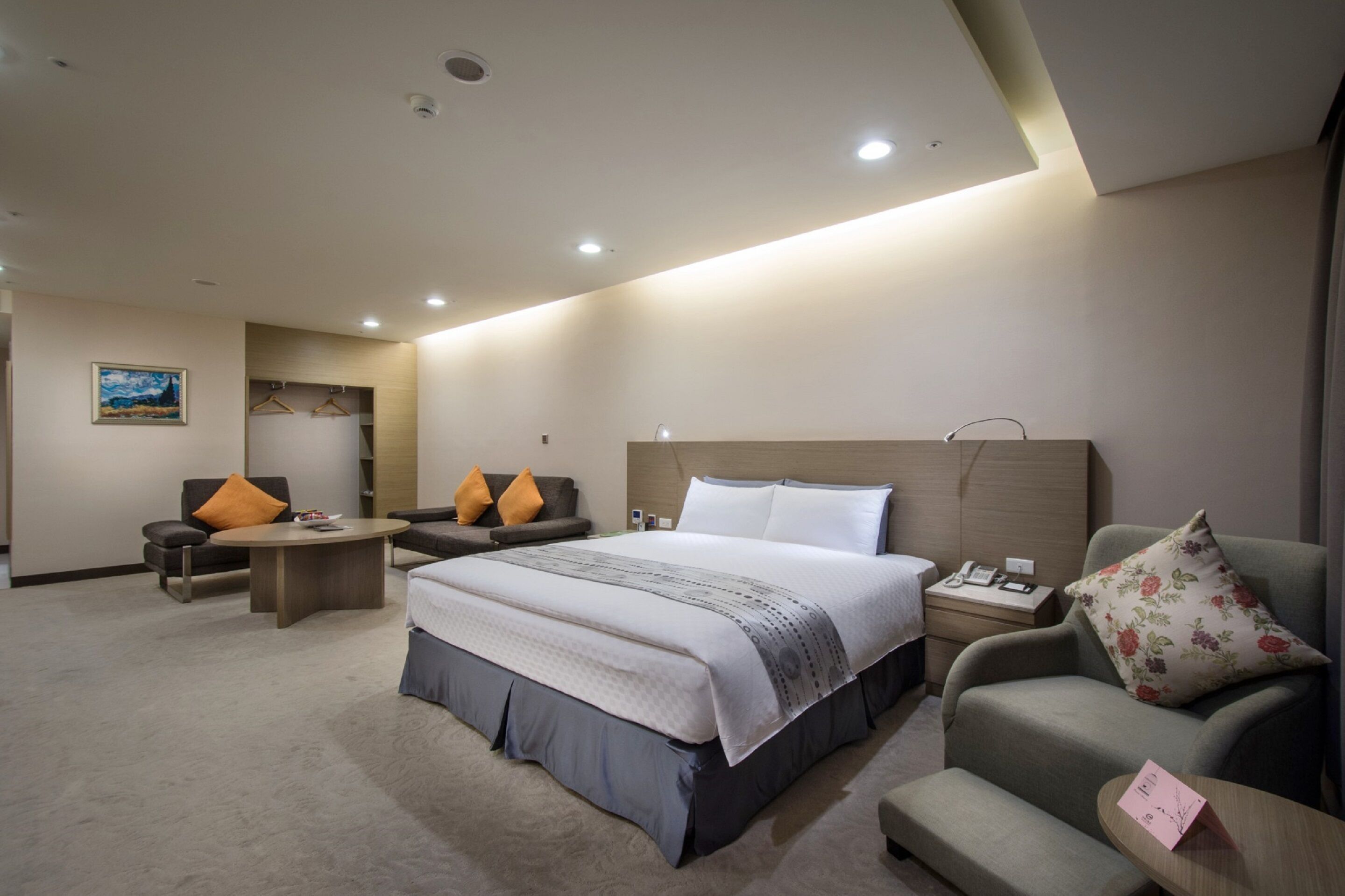 A modern hotel room with a large bed, two armchairs, a small table, and a nightstand.