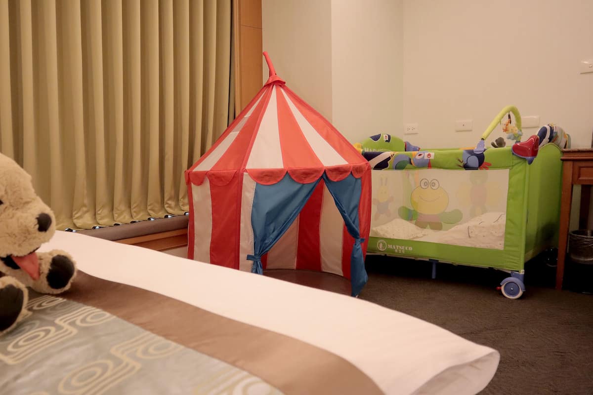 A hotel room with a bed, a small tent, a crib, and a plush toy.
