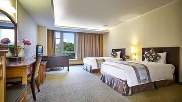 A hotel room with two beds, a desk, a chair, a television, and a window with curtains.